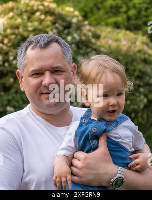 Porträt eines Vaters und eines kleinen Sohnes. Ein glücklicher Vater hält ein kleines Baby mit welligen, blonden Haaren in den Armen. Das Kind ist ein Jahr alt. Nahaufnahme Stockfoto