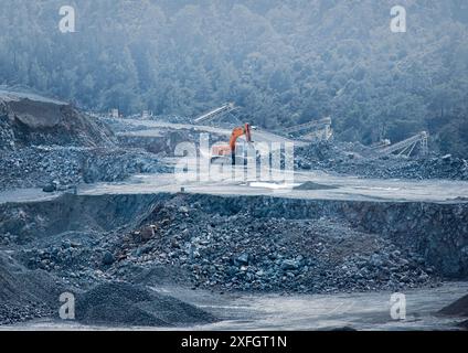 Bagger, der in einem Diabasisbruch mit Förderbändern und Wald im Hintergrund betrieben wird. Steinbruch Parekklisia, Zypern Stockfoto