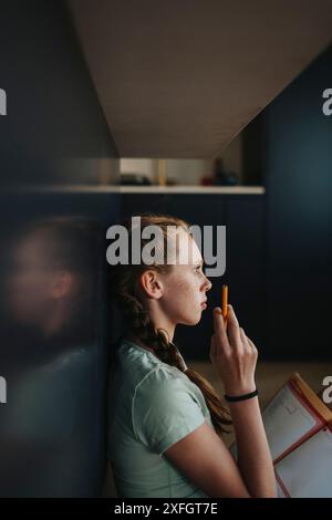 Nachdenkliches Mädchen, das sich auf den Tisch lehnt, während es zu Hause studiert Stockfoto