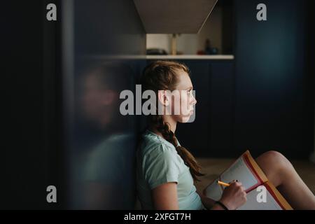 Ein nachdenkliches Mädchen sitzt auf dem Boden, während er zu Hause studiert Stockfoto