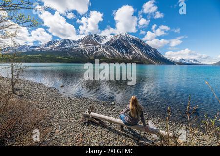 Touristen, Wanderer, der im Sommer neben dem atemberaubenden See im Norden Kanadas sitzt, mit schneebedeckten Bergen im Hintergrund, unberührtem See, felsigem See. Stockfoto