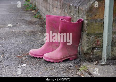 Ein Paar wellington-Kinderstiefel vor der Haustür. Pinkfarbene Schuhe für nasses Wetter Stockfoto