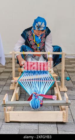 Almaty, Kasachstan - 20. März 2024: Asiatische Handwerkerin in traditioneller kasachischer Kleidung mit Stickerei, die einen schmalen Teppich aus Wollfäden aufzieht Stockfoto