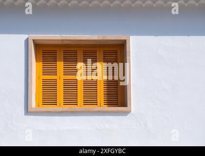 Kleines Fenster mit gelben Holzläden an einer weißen Wand. Stockfoto