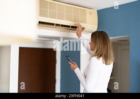 Frau steuert eine intelligente Klimaanlage mit einer Fernbedienung auf ihrem Telefon. Stockfoto