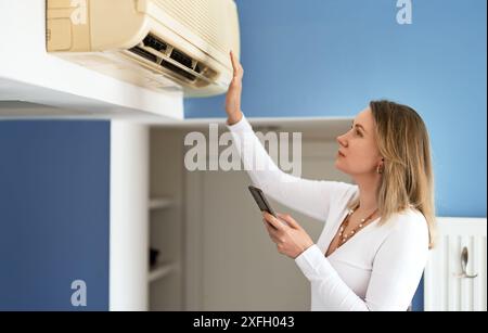 Frau steuert eine intelligente Klimaanlage mit einer Fernbedienung auf ihrem Telefon. Stockfoto