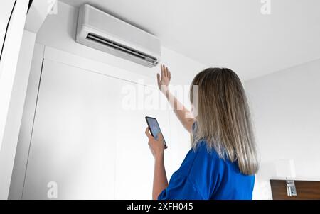 Frau steuert eine intelligente Klimaanlage mit einer Fernbedienung auf ihrem Telefon. Stockfoto