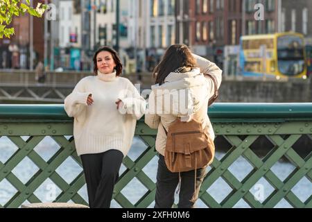 Straßenporträt von Dublins Frau. Brünette Frau in weißem Pullover posiert auf der Brücke und Freund fängt sie mit Kamera am Fluss ein. Dublin, Irland. Stockfoto