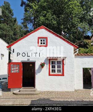 Ein bezauberndes weiß-rotes Gebäude mit „Politi“-Schild, umgeben von Grün und klarem Himmel, das eine malerische Polizeistation in einer malerischen Umgebung darstellt Stockfoto