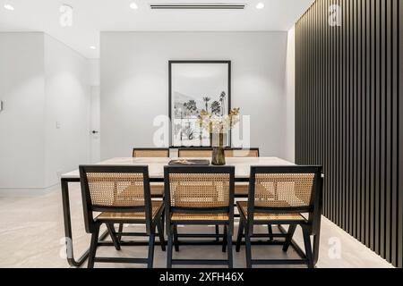 Ein moderner Speisesaal mit minimalistischem Design, Holztisch, Korbsessel und dekorativer Vase in einer gut beleuchteten Inneneinrichtung. Stockfoto