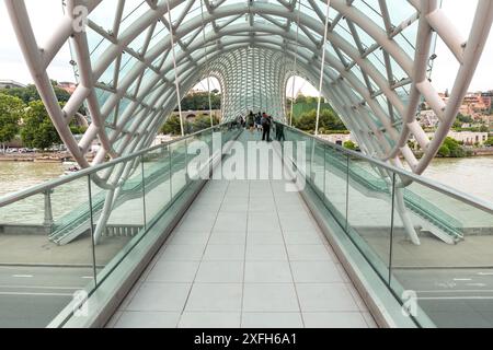 Tiflis, Georgien – 17. Juni 2024: Die Friedensbrücke ist eine bogenförmige Fußgängerbrücke, eine Stahl-Glas-Konstruktion über den Fluss Kura, die die Brücke verbindet Stockfoto