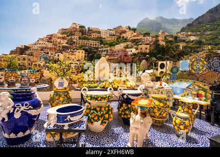 Positano, Italien - 29. Juni 2024: Ein Blick auf farbenfrohe Vasen-Dekorationsgegenstände vor der wunderschönen Landschaft von Häusern auf einem Hügel Stockfoto