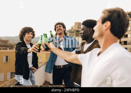 Fröhliche männliche Freunde, die Bierflaschen auf Party auf dem Dach des Gebäudes tosten Stockfoto