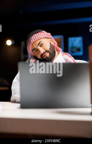 Detaillierte Ansicht eines muslimischen Mannes, der sich auf einen Anruf konzentrierte, während er seinen Laptop untersuchte. Professionalität und ausgezeichnete Kommunikation werden am Beispiel einer arabischen Person veranschaulicht, die Technologie liebt. Nahaufnahme. Stockfoto