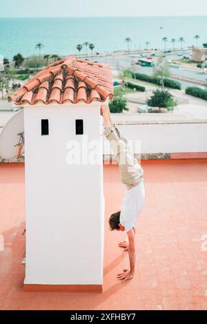 Die ganze Länge eines Mannes, der auf der Terrasse des Gebäudes einen Handstand macht Stockfoto