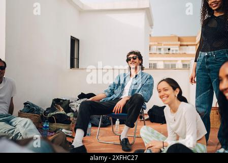 Ein lächelnder Mann sitzt mit männlichen und weiblichen Freunden auf dem Dach Stockfoto