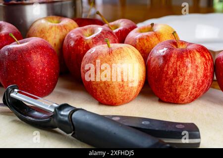 Ein Messer und Schäler auf einem weißen Schneidebrett, umgeben von Gala-Äpfeln. Vorbereitung für einen Kuchen... Stockfoto