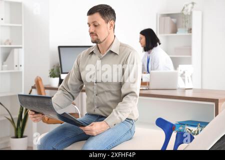 Junger Mann mit Röntgenbild der in der Klinik sitzenden Wirbelsäule Stockfoto