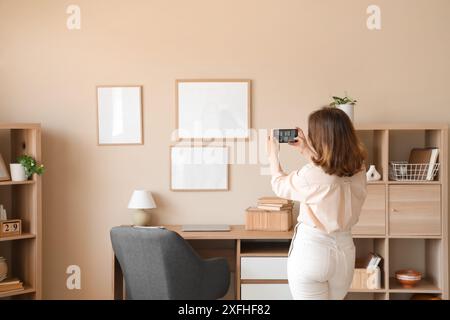 Junge Frau, die zu Hause leere Rahmen an beigefarbene Wand aufgehängt hat Stockfoto