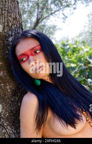 Porträt einer gebürtigen brasilianischen Frau mit traditioneller Gesichtsfarbe in einer üppigen Waldlandschaft. Stockfoto