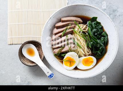 Eine Schüssel Ramen mit Rindfleischscheiben, weich gekochten Eierhälften und grünem Gemüse. Die Mahlzeit wird mit grünen Zwiebeln garniert Stockfoto