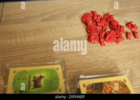 Mozyr, Weißrussland, 10. April 2024: Red Meeple Game Elements for Catan Board Game on Beige Background Chip Distribution. Stockfoto