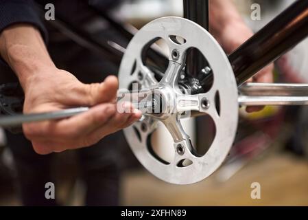 Wartung eines Fahrrads: Hände einer nicht erkennbaren Person, die die Pedale eines Fahrrads in seiner Werkstatt montiert. Echte Menschen bei der Arbeit. Stockfoto