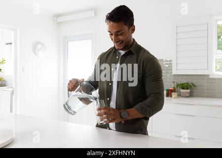 Ein Lächeln, ein Mann, der Wasser aus dem Krug in der modernen Küche gießt Stockfoto