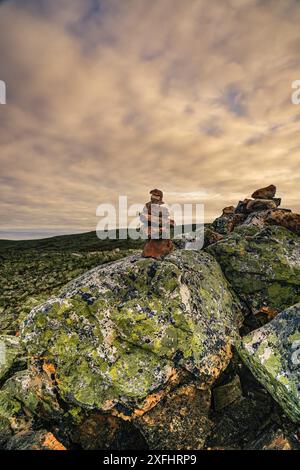 Der Steinkairn befindet sich auf einem großen, moosbedeckten Felsen auf dem Nipfjället-Gipfel in Idre, Dalarna, Schweden. Hintergrund eines bewölkten Sonnenaufgangshimmels Stockfoto