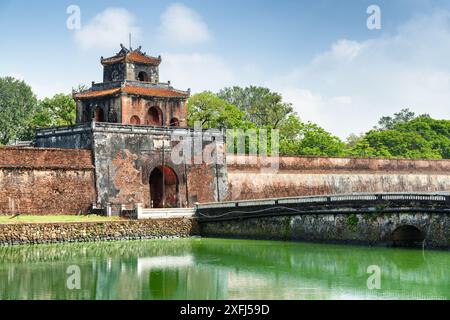 Malerischer Blick auf das Ngan-Tor in der Festungsmauer der Zitadelle und eine Brücke über den Graben rund um die Kaiserliche Stadt mit der lila Verbotenen Stadt, Hue, Stockfoto