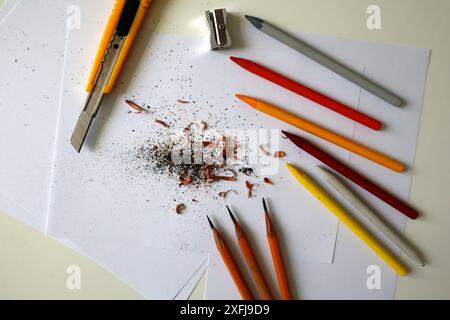 Fotoschärfen verschiedener Bleistifte. Buntstifte in verschiedenen Farben, Schreibwarenmesser, Bleistiftspitzer. Späne von Bleistiften. Papier, weißer Hintergrund Stockfoto