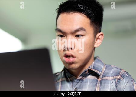 Ein junger männlicher Student im Teenageralter konzentriert sich auf seinen Laptop-Bildschirm und lernt im Klassenzimmer mit interaktiver Technologie Stockfoto