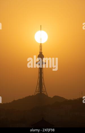 Eine Silhouette eines Turms mit Sonnenuntergang dahinter, die einen dramatischen goldenen Himmel in Qingdao, China, schafft Stockfoto