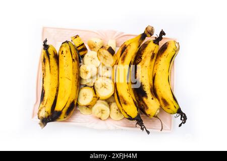 Frische Bananen auf Teller auf weißem Hintergrund. Selektiver Fokus, Bananenbündel und eine geschnittene Banane auf Vintage-Holzhintergrund, selektiver Fokus Stockfoto