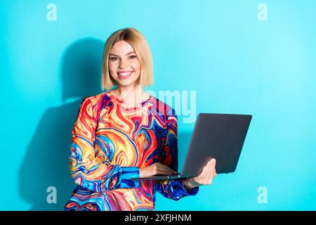 Foto des klugen optimistischen netten Mädchens mit bob Friseur gekleidetes Druckhemd halten macbook Laptop in den Händen isoliert auf blauem Farbhintergrund Stockfoto