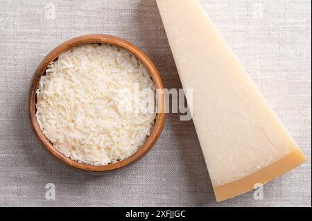 Geriebener Parmesankäse, Parmigiano Reggiano oder Grana Padano in einer Holzschale auf Leinen, mit dem ganzen Stück auf der rechten Seite. Italienischer Hartkäse mit Granulat. Stockfoto