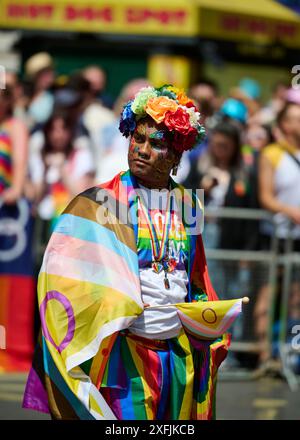 Eine Person, die in leuchtenden Regenbogenfarben und Blumen gekleidet ist, nimmt an einer Stolz-Parade Teil Stockfoto