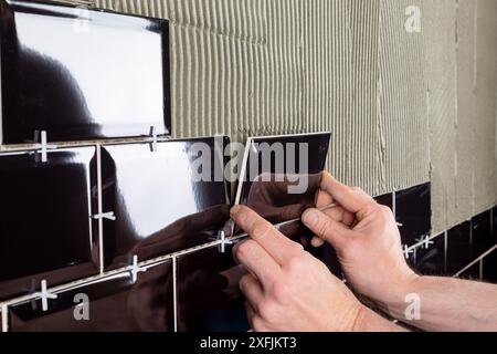 Verlegung von Wandfliesen mit schwarzen glänzenden Fliesen im Metro-Stil auf flexiblem Zementkleber. DIY Küche Bad Renovierung Installation und Bauingenieur Stockfoto