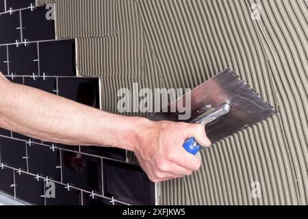 Verlegung von Wandfliesen mit schwarzen glänzenden Fliesen im Metro-Stil auf flexiblem Zementkleber. DIY Küche Bad Renovierung Installation und Bauingenieur Stockfoto