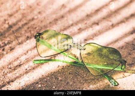 Grüne herzförmige Sonnenbrille liegen am Sandstrand an sonnigen Sommertagen Urlaub am Meer, Meer in tropischem Resort. Im Sommer entspannen Sie sich im Spa-Resort Stockfoto