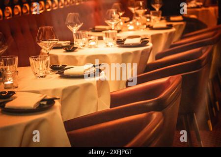 Abends werden Tische mit weißen Tischdecken mit Besteck, Tellern, Gläsern und Servietten in einem luxuriösen Restaurant serviert. Leere Sitze auf einem Tisch. Stockfoto