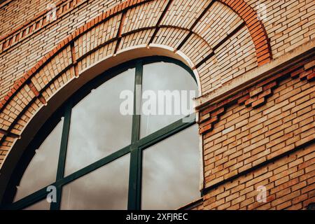 Die Seite eines verlassenen Fabrikgebäudes mit roter Backsteinmauer und gewölbtem großen Fenster. Altes Haus. Klassische Architektur. Hochwertige Fotos. Stockfoto