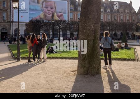 Menschen hängen am Place des Vosges in Paris ab, mit einer Apple-Werbung, die auf sie herabblickt. Stockfoto