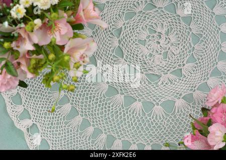 Weiße und mintfarbene Tischdecke, regionales Häkelmuster mit rosafarbenen Blumen. Geringe Schärfentiefe. Stockfoto