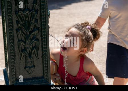 Aufnahme eines kleinen Mädchens, das im Sommer einen erfrischenden Moment mit ihrem Spielzeug in einem Brunnen genießt. Freude und Kühle draußen. Stockfoto