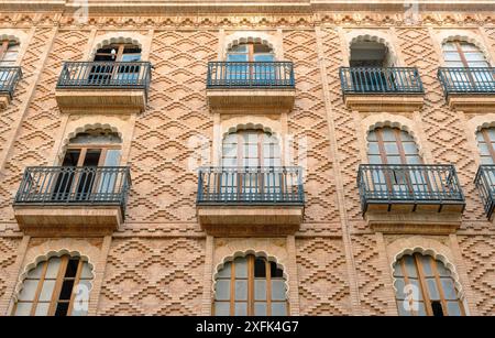 Detaillierter Blick auf eine Backsteinfassade mit Bogenfenstern und schmiedeeisernen Balkonen. Das komplizierte Ziegelwerk und das elegante Design spiegeln historische Architektur wider. Stockfoto