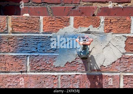 Wasserhahn mit blauer Farbe an einer Ziegelwand Stockfoto