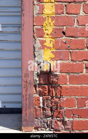 Beschädigte Ziegelwand mit gelber Farbe neben der hochrollbaren Metalltür Stockfoto