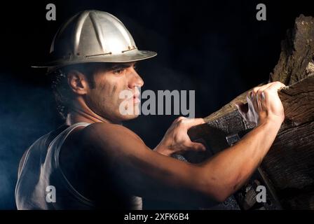 Porträt eines jungen Mannes mit einem verschmierten Gesicht und einem alten Aluminiumhelm in einer Mine mit den Händen auf einem Holzminenkarten Stockfoto