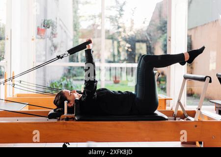 Junge und fitte Frau trainiert Pilates auf Reformerbett. Reformer Pilates Studio-Gerät für Fitnessübungen im Fitnessstudio. Fitnesskonzept. Gesund und s Stockfoto